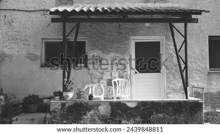 Rustic Home Entrance In Monochrome, Time-Worn Patio With Potted Plants And Plastic Chairs Royalty-Free Stock Photo #2439848811