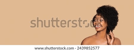 Radiant young black woman with curly natural hair looking away at free space with joyful smile, posing on beige background, embodying natural beauty, advertisement banner