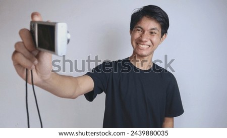 Young Asian man enjoys taking selfies using a pocket camera on an isolated white background