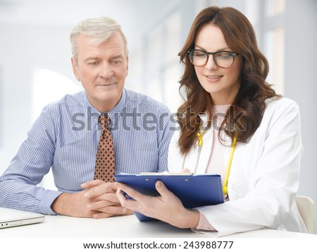 Female doctor consulting with senior patient while sitting at desk at clinic.