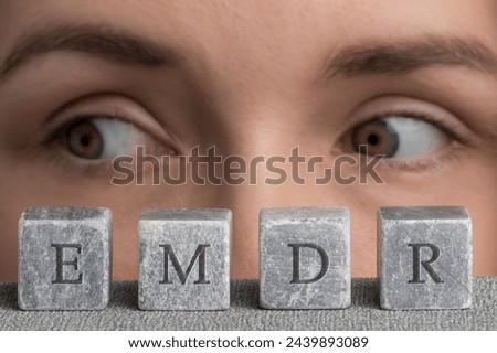 Eye Movement Desensitization and Reprocessing psychotherapy treatment concept. Letters EMDR written on grey stone cubes blocks. Close-up woman's face with eyes looking right. Royalty-Free Stock Photo #2439893089