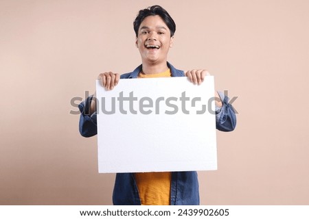 Happy young Asian man showing and displaying placard ready for your text or product