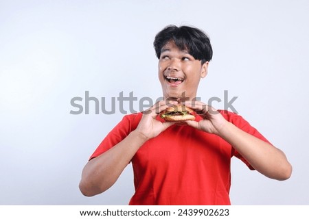 Cheerful young man looking aside to the empty space for ads while holding a burger