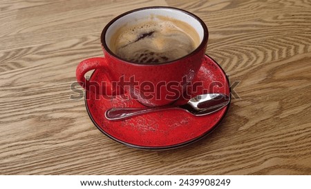 A red cup of coffee with foam on the table, featuring an elegant and luxurious ceramic design in the style of an elegant and luxurious ceramic artist, next to it is a spoon placed on its plate