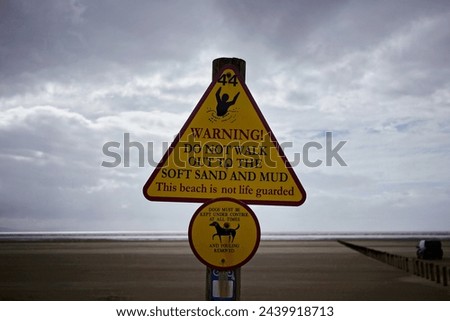 View of generic warning signs on a beach with stormy skies above - the sign warns off quicksand