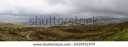 A panoramic view from the heights of Isle of Skye presents a tapestry of heathlands with meandering trails leading to the vast, shadowy waters of the Sound of Raasay Royalty-Free Stock Photo #2439921979