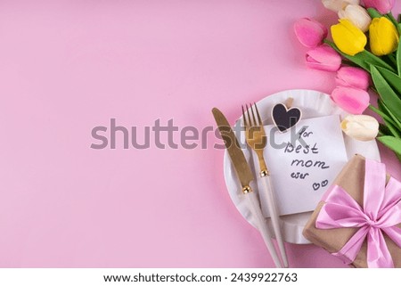 Mother day table setting background. Pink Mother's day border flat lay for brunch, lunch, dinner menu, invitation mockup. Beautiful table setting with golden cutlery, plate, tulip flowers and gift box Royalty-Free Stock Photo #2439922763