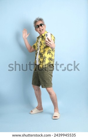 HAPPY SONGKRAN DAY. Asian tourist senior man in summer clothing with gesture of  taking a selfie isolated on blue background. Songkran festival. Thai New Year's Day.