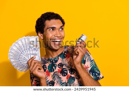 Photo of wealthy young guy tourist holding banknotes advertising and looking betting company copyspace isolated on yellow color background