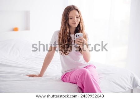 Photo of positive peaceful girl sit comfy bed use smart phone chatting bright interior bedroom apartment indoors