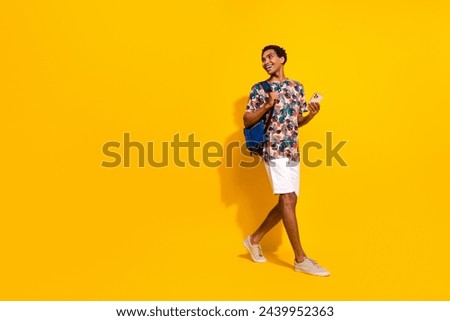 Full length photo of positive man wearing casual summer outfit bring phone and backpack look copyspace isolated on yellow color background