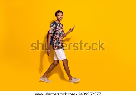 Full body length size photo of young guy strolling tourist with backpack use smartphone browsing news isolated on yellow color background