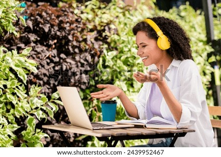 Photo of cute cheerful woman dressed white shirt earphones sitting cafe video call modern gadget outdoors urban city park