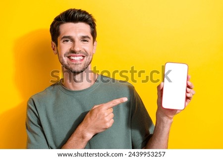 Photo of intelligent pleasant man dressed khaki t-shirt directing at smartphone display empty space isolated on yellow color background