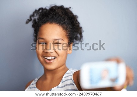 Young girl, selfie and wink in studio for happiness, closeup and vibrant teen by grey background. Child, smile and excited teenager with profile picture, technology and update on social media