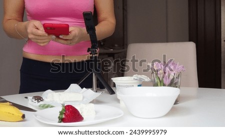 girl blogger films breakfast for video blog, content for social networks, stories. Hands with the phone close-up pictures of food. Breakfast for two : yogurt, coffee, fruit ,  strawberry, banana