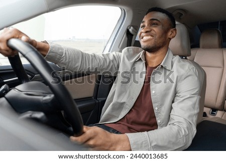  Portrait of happy african american man driving car with beige interior Royalty-Free Stock Photo #2440013685