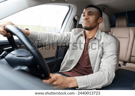  Portrait of a serious african american man driving a car with a beige interior Royalty-Free Stock Photo #2440013723