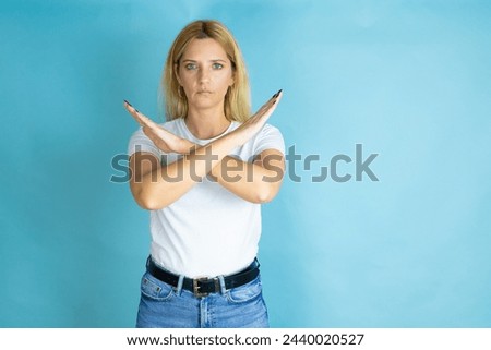 Young beautiful woman wearing casual t-shirt over isolated blue background Rejection expression crossing arms doing negative sign, angry face Royalty-Free Stock Photo #2440020527
