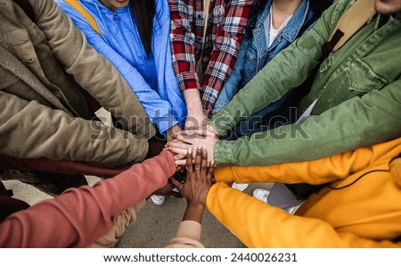 Diverse group of young friends stacking hands outdoors showing support and unity. Community and youth concept.