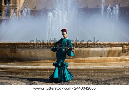 Beautiful young woman in a green frilly suit with a flower on her head. The woman is dancing flamenco and is in the most famous square in seville, spain, in front of its central fountain Royalty-Free Stock Photo #2440042055