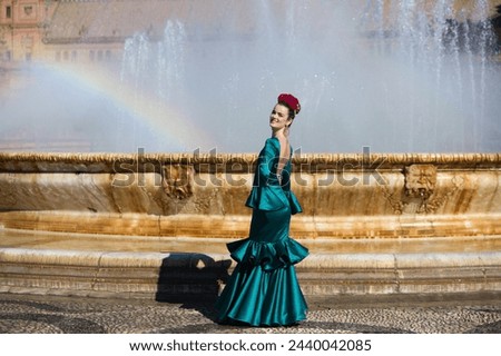 Beautiful young woman in a green frilly suit with a flower on her head. The woman is dancing flamenco and is in the most famous square in seville, spain, in front of its central fountain Royalty-Free Stock Photo #2440042085