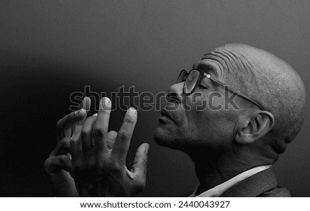 man praying to god with hands together Caribbean man praying with grey black background stock photo