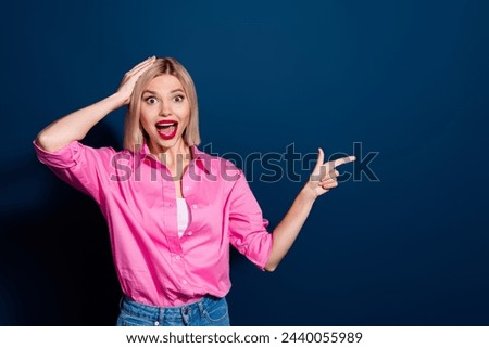 Photo of crazy funky ecstatic girl dressed pink shirt indicating at sale empty space arm on head isolated on dark blue color background