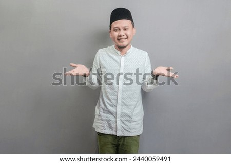 Happy asian muslim man hinking worried about a question or confused wearing a koko shirt and peci with shades of the fasting month, isolated on a gray background