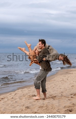 Man carrying woman piggyback on beach, both smiling. Image captures fun, affection, ideal for themes of love or joyful moments and the happiness of weeding or engagement. High quality photo