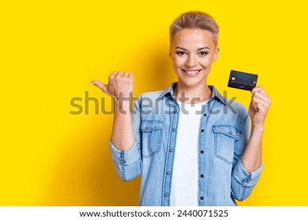 Photo portrait of lovely young lady hold credit card point empty space wear trendy jeans garment isolated on yellow color background