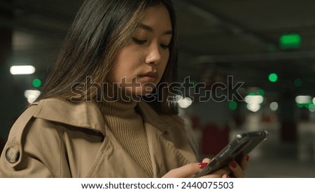 Serious Asian woman chinese korean japanese woman girl ethnic lady client customer driver in underground car parking chatting mobile phone application typing message browsing internet cellphone chat Royalty-Free Stock Photo #2440075503