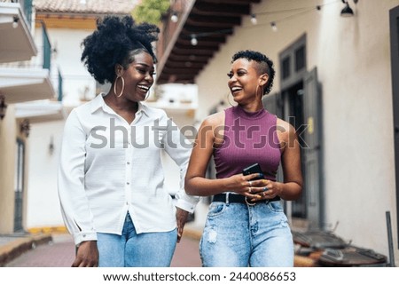 Black women stylish friends having fun walking down the street while using smartphone