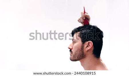 Young man dyes his hair with natural dark brown dye to cover his gray hair. Henna based hair dye. Profile view with white background.