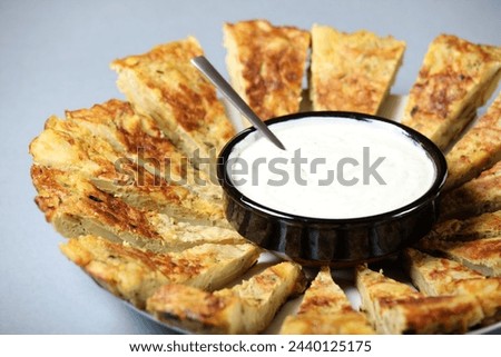 A picture of a typical Spanish tortilla with a garlic dip over light background