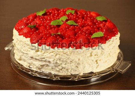 A picture of meringue cake decorated with fresh strawberries redcurrant and mint leaves