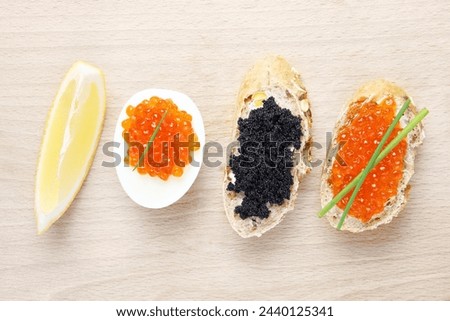 A picture of red and black caviar served on a baguette and an egg with lemon on a wooden board