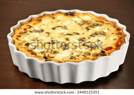 A picture of freshly baked vegetable quiche in a white tin over wooden surface
