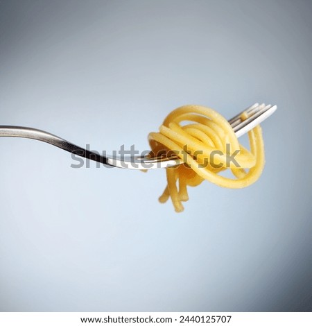 A picture of a silver fork with spaghetti noodle over grey background