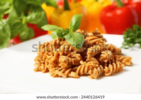 A picture of Italian pasta with red pepper pesto served on a white plate and decorated with basil