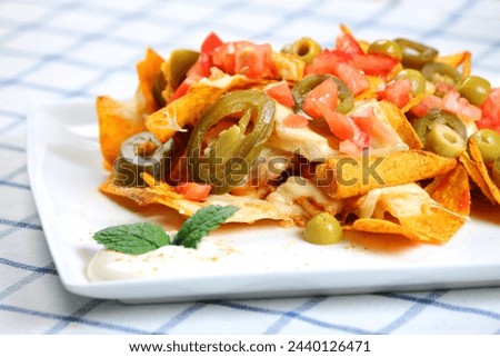 A picture of chicken nachos served on a white plate with sour cream