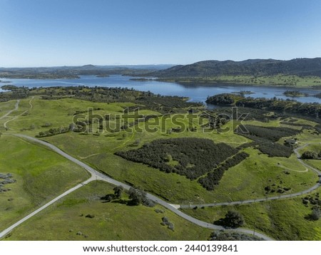 Drone image over beautiful rolling green hills in Northern California with New Hogan Lake in the background and a blue sky