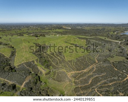 Drone image over beautiful rolling green hills in Northern California with New Hogan Lake in the background and a blue sky