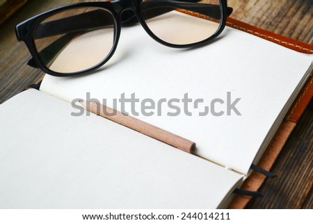 An empty retro notebook with old paper, little pencil, glasses and leather cover
