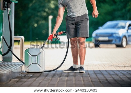 Handsome driver refueling canister with gasoline at modern gas station. Man filling cistern with fuel in case of unforeseen circumstances. Cropped view of man with pump nozzle on background of his car Royalty-Free Stock Photo #2440150403