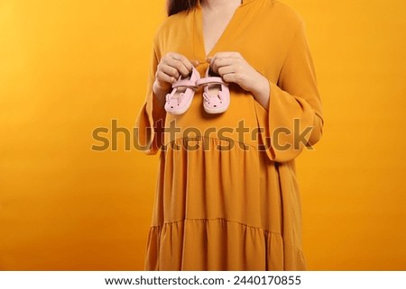 Pregnant woman with baby shoes on yellow background, closeup