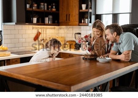 A heartwarming scene unfolds as a family relishes a mouthwatering chocolate cake together in the warmth of their sunlit kitchen, sharing smiles and creating memories Royalty-Free Stock Photo #2440181085