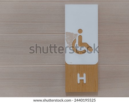 A restroom sign for handicapped person on a brown wood panel.
