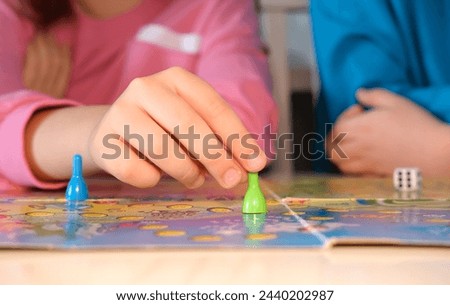 Board game and children's leisure concept - little child's hand holds green piece in its hand over game board. Selective focus.