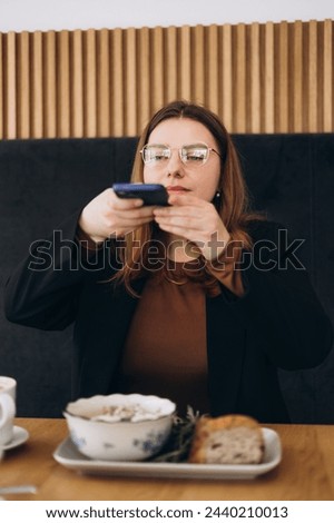 Female blogger influencer hold phone take food mobile photo on phone sit at cafe table. Woman vlogger shoot social media post on smartphone closeup view.